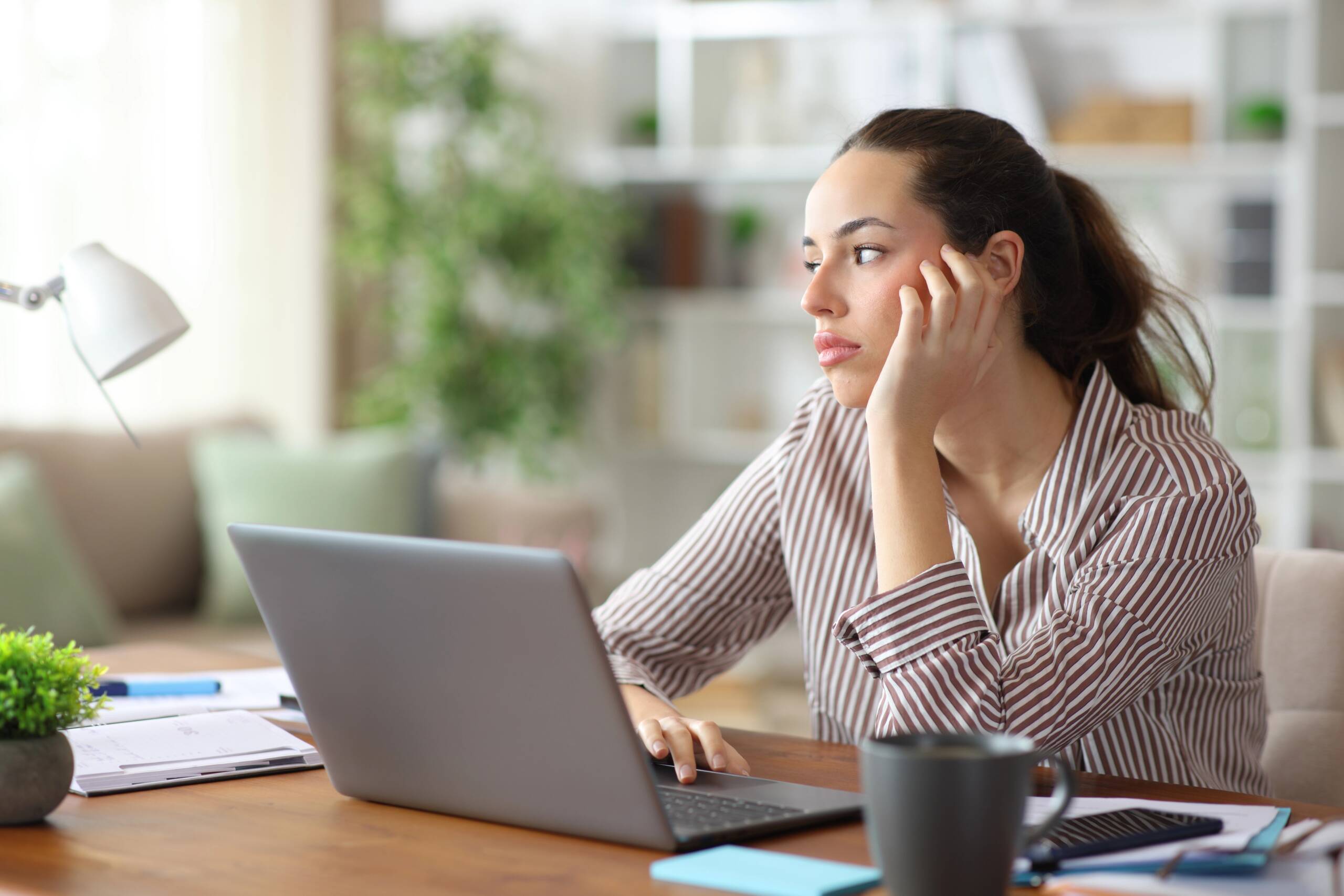 Professional woman working on a laptop at home, looking tired and distracted