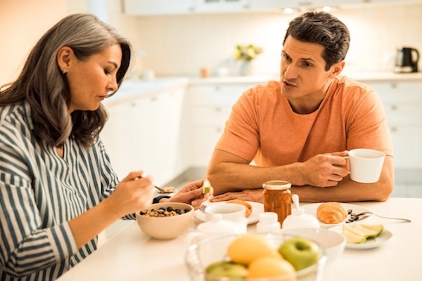 Couple at home talking while one partner appears distracted and looking down