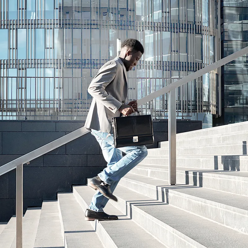 High achieving young man in professional attire with briefcase running up stairs outside in an urban business area